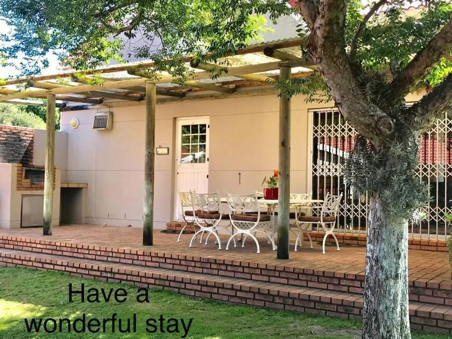 Shaded pergola patio with white chairs and mature tree overhead