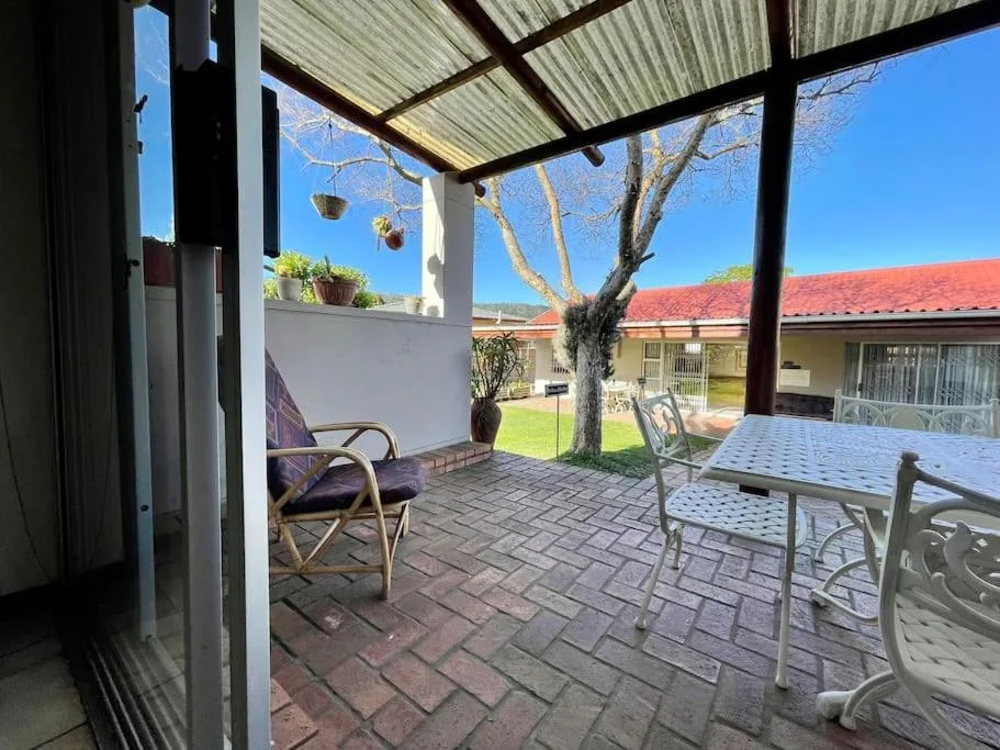 Covered patio with seating, large tree, and garden views