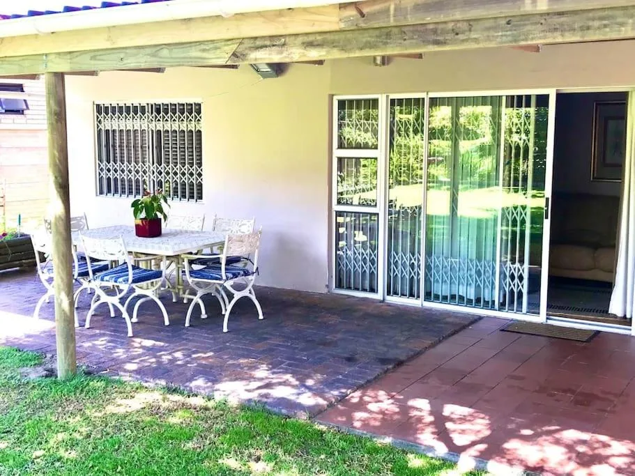 Covered patio with dining table, white chairs, and glass sliding doors