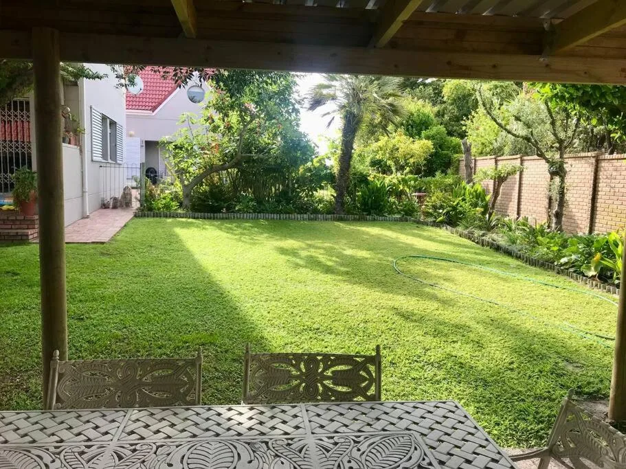 Covered patio with seating overlooking spacious green lawn and garden