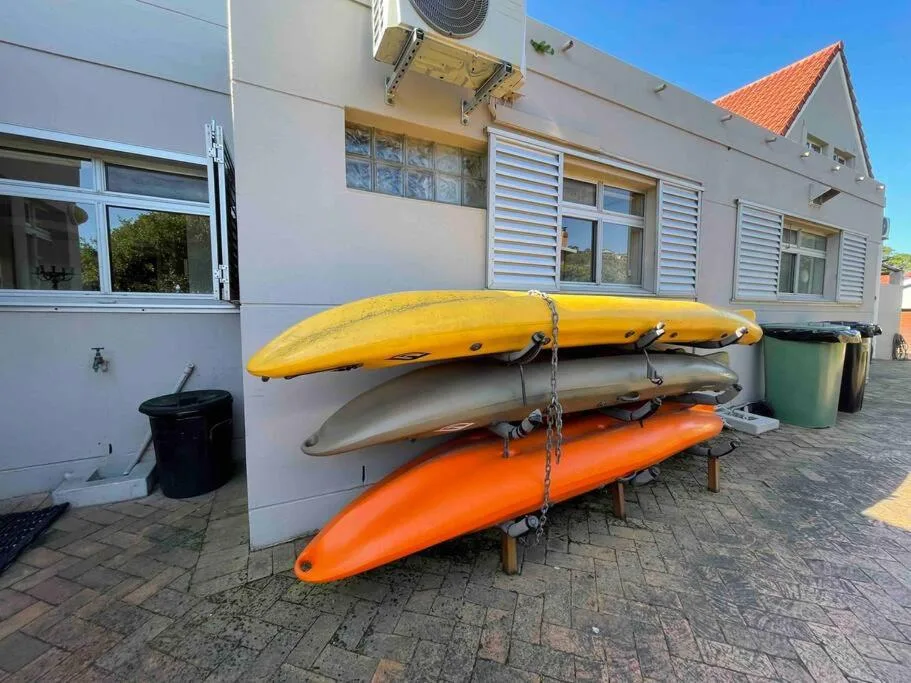 Three colorful kayaks stacked against white cottage exterior wall