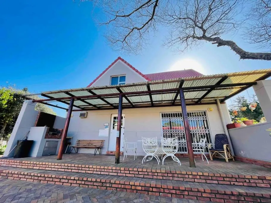 White cottage with red roof and pergola patio, brick driveway, clear blue sky