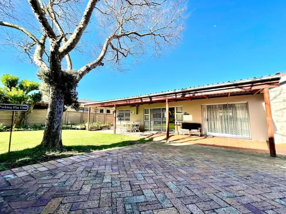 Single-story cottage with covered porch and mature tree in landscaped garden