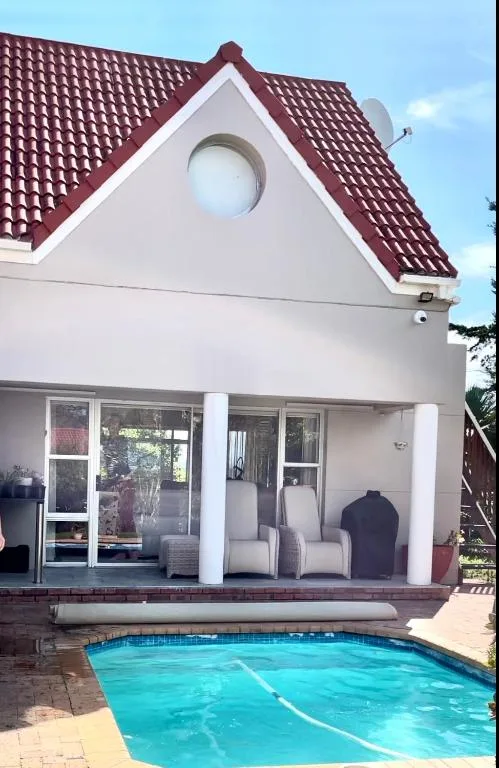 Swimming pool with turquoise water in front of white cottage with burgundy roof
