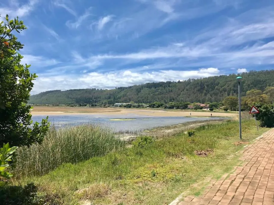 Scenic lagoon view with forested hills, sandy beach, and blue sky