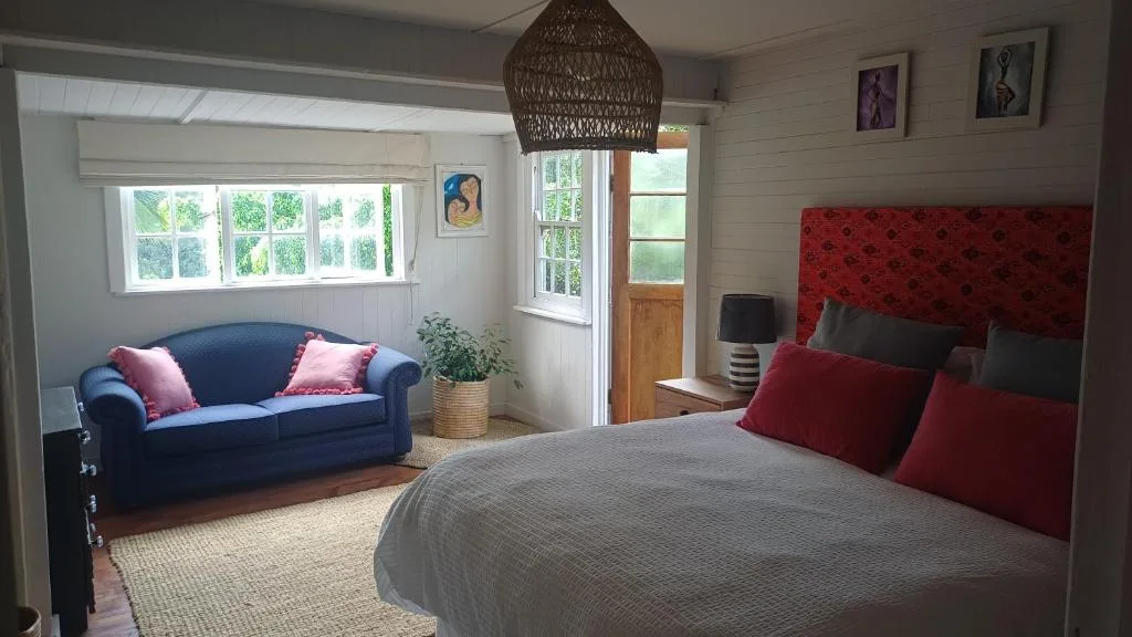 Spacious bedroom with queen bed, blue sofa, and garden views through windows