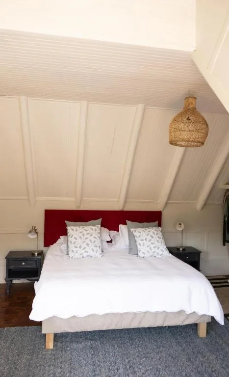 Bright bedroom with red headboard, white linens, and woven pendant light