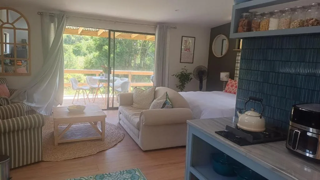 Bright bedroom with bed, armchair, kitchenette, and deck access overlooking garden