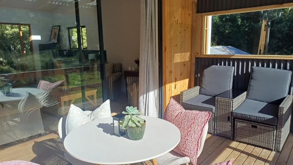 Wooden deck with white table, cushioned chairs, and garden views