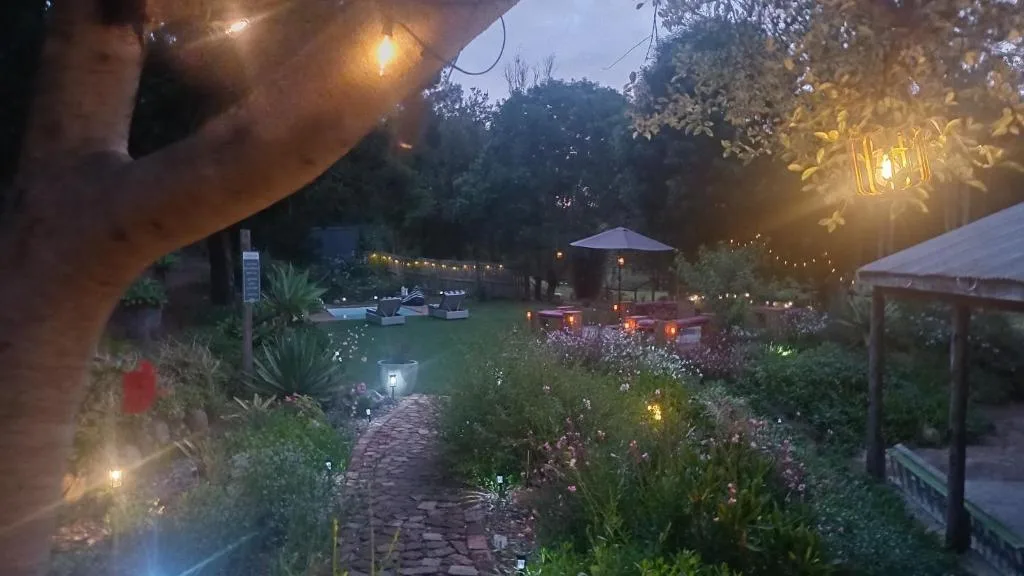 Evening garden pathway with glowing lights, lush landscaping, and distant pool area