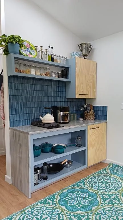 Modern kitchenette with blue tile backsplash, open shelving, and wooden cabinetry