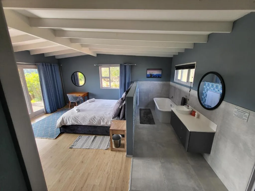Modern bedroom with en-suite bathroom, bed, and garden views through glass doors