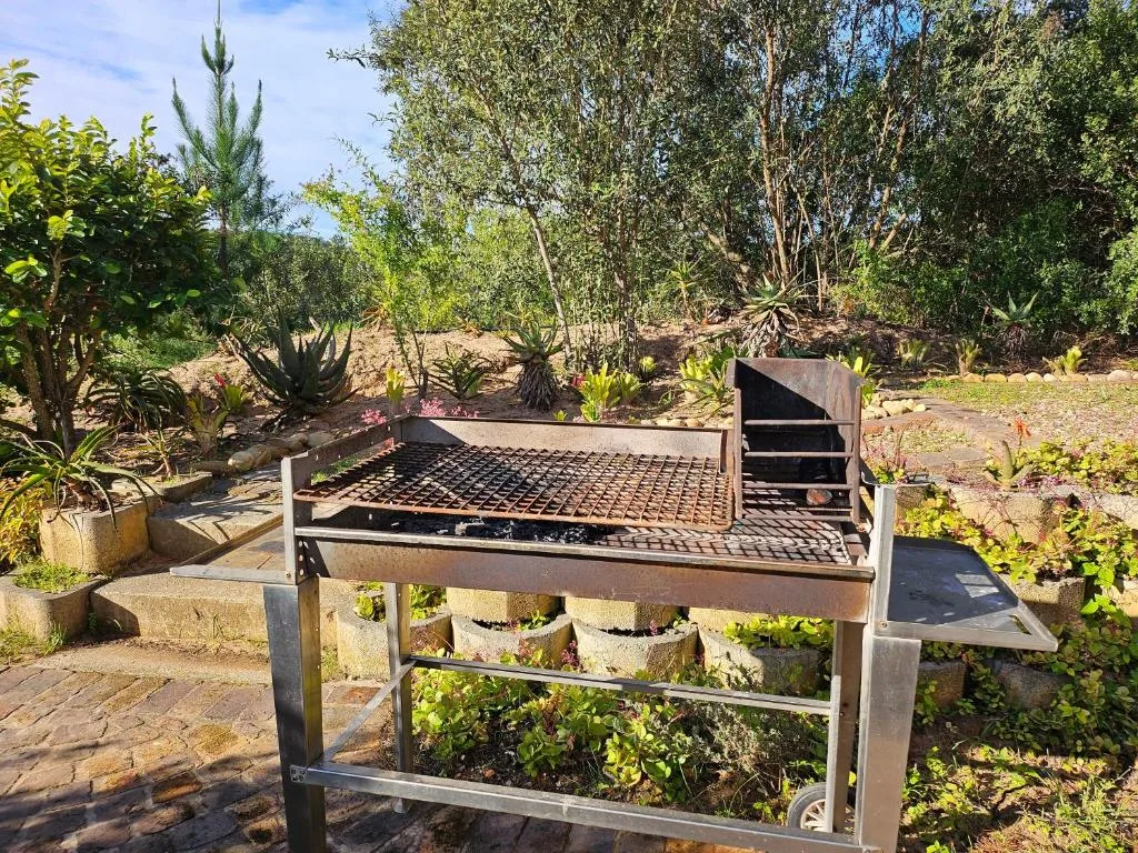 Metal braai grill in landscaped garden surrounded by native plants and trees