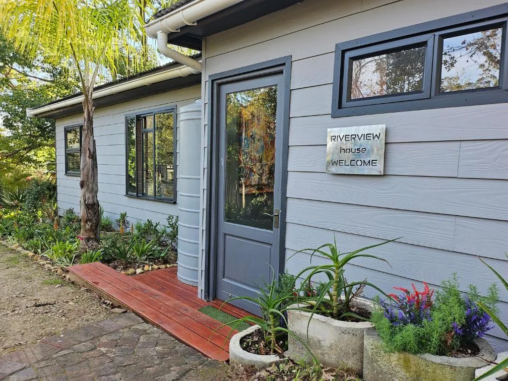 Modern cottage exterior with welcoming sign and lush garden plantings