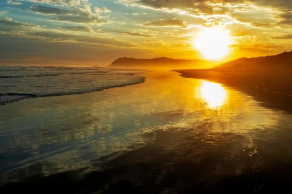 Golden sunset over ocean and beach with mountains in distance