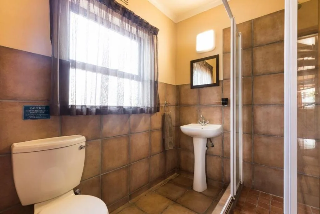 Bathroom with toilet, pedestal sink, shower enclosure, and brown tile walls