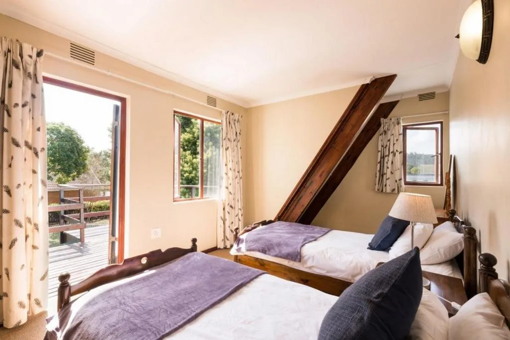 Bright bedroom with two wooden beds, purple throws, deck access and windows