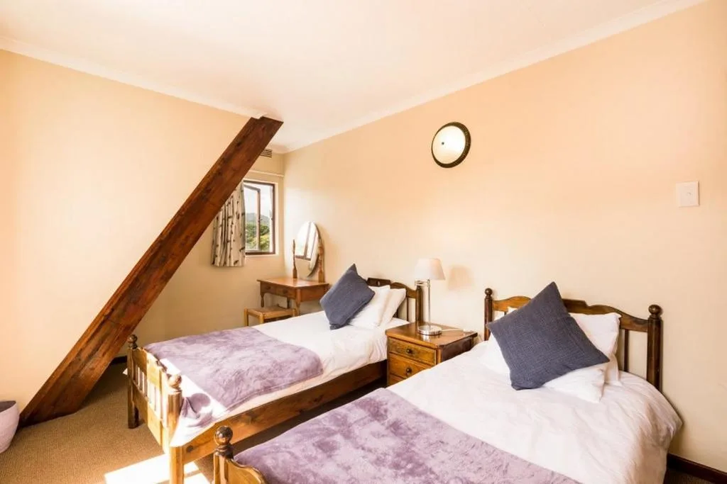 Twin bedroom with wooden beds, purple quilts, and dark pillows under sloped ceiling