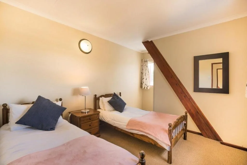 Twin bedroom with wooden beds, navy pillows, and wooden staircase