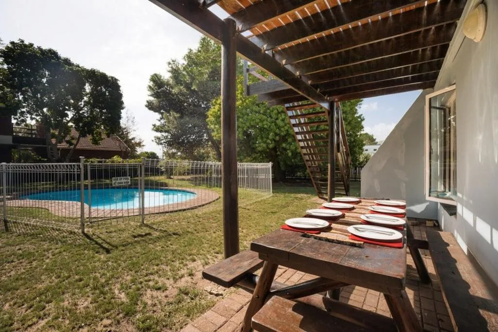 Covered patio with picnic table and fenced pool in garden background