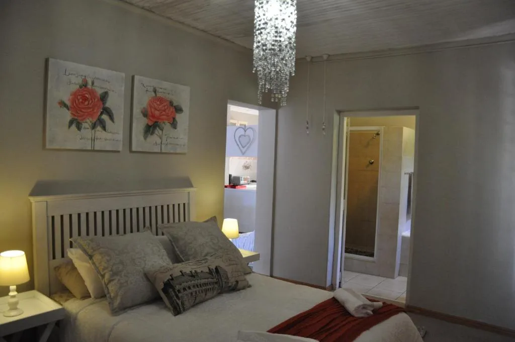 Bright bedroom with made bed, floral artwork, crystal chandelier, and en-suite access