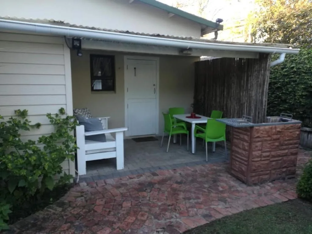 Outdoor patio with dining table, green chairs, and braai area