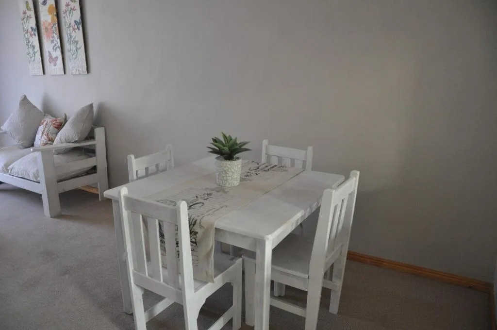 White wooden dining table with four chairs and potted plant centerpiece