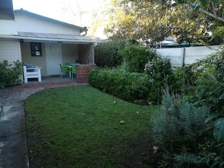 White cottage with brick patio, green lawn, and lush garden surroundings
