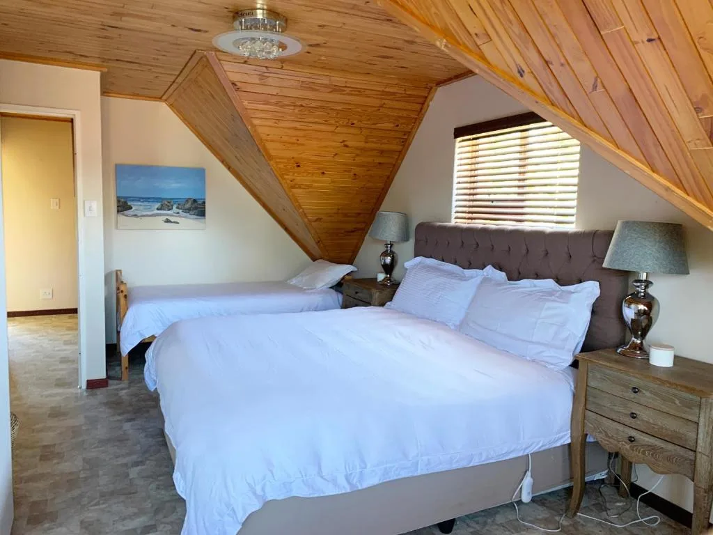 Bright attic bedroom with queen bed, wooden ceiling, and coastal artwork
