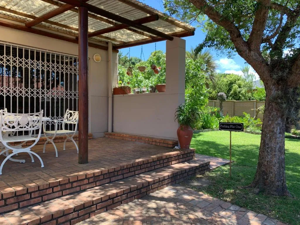 Brick patio with pergola, white chairs, lush garden, and mature tree