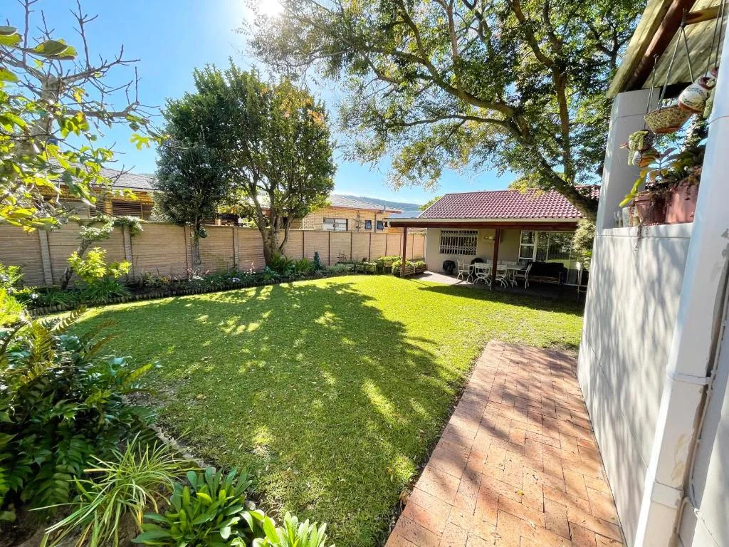 Spacious garden with manicured lawn, mature trees, and covered patio area