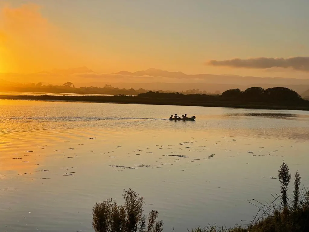 Golden sunset over tranquil lagoon with distant mountains and silhouetted trees