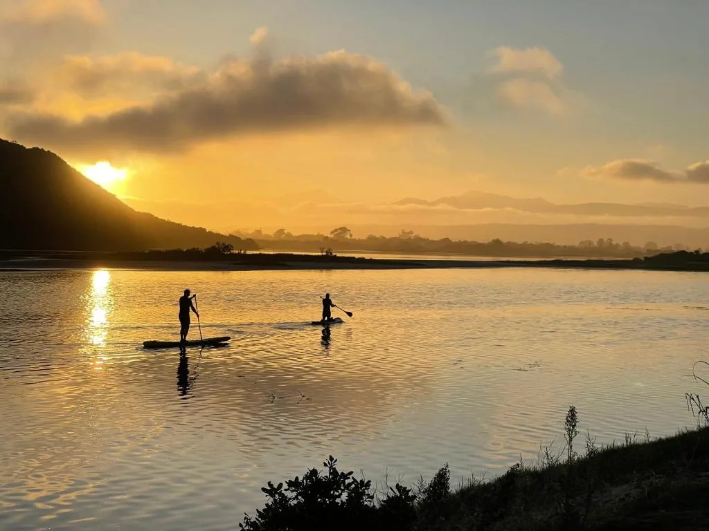 Sunset over lagoon with paddleboarders and mountain silhouette