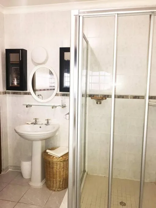Clean bathroom with pedestal sink, round mirror, and enclosed shower cubicle