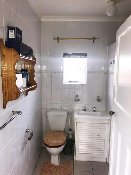Compact bathroom with toilet, sink, shower, and decorative wooden shelf