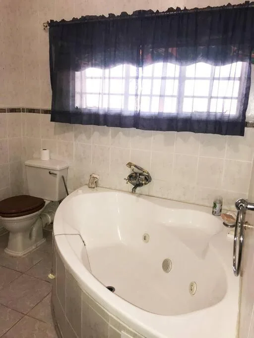 Bathroom with white jacuzzi tub, toilet, and window with dark curtains