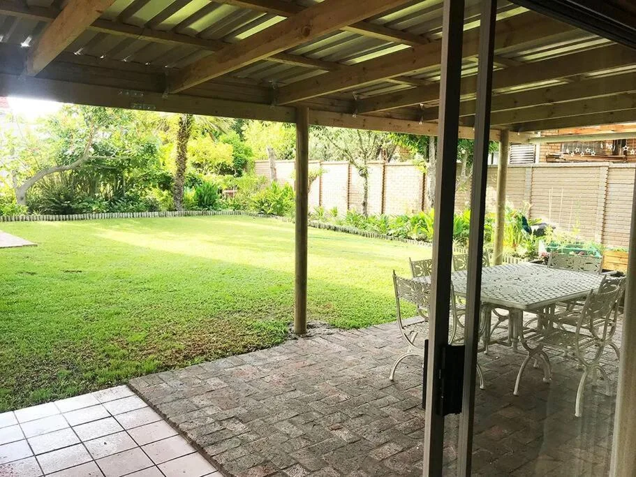 Covered patio with dining table overlooking manicured lawn and garden