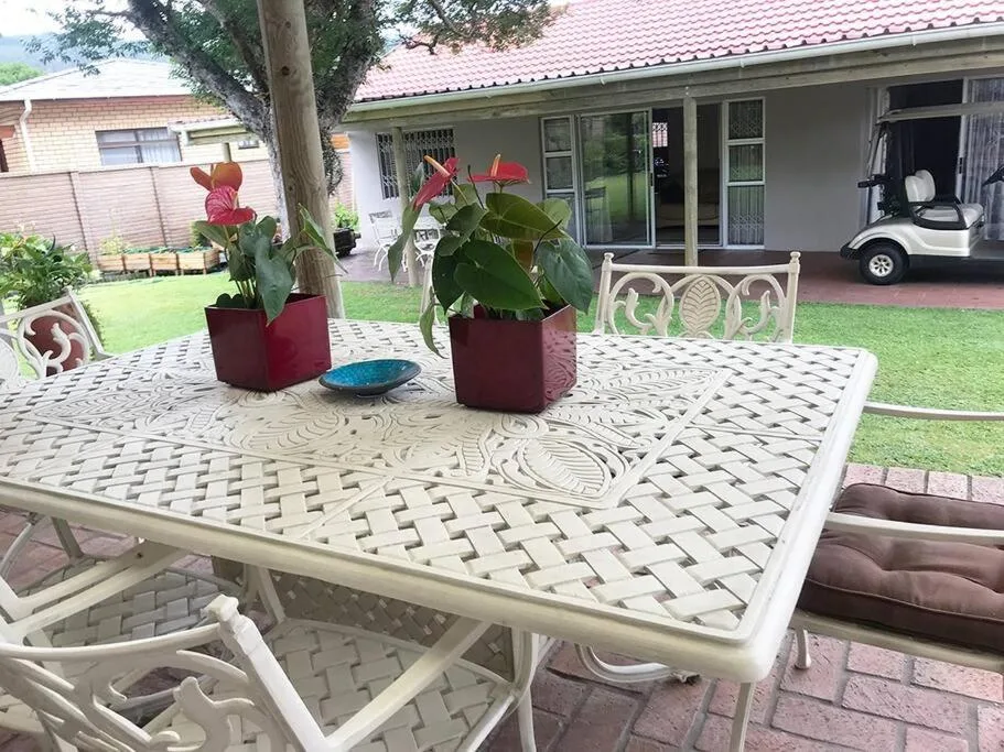 Outdoor patio with dining table, chairs, potted flowers, and lawn view