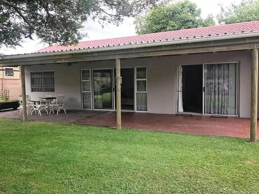 Covered patio with dining furniture overlooking manicured garden lawn