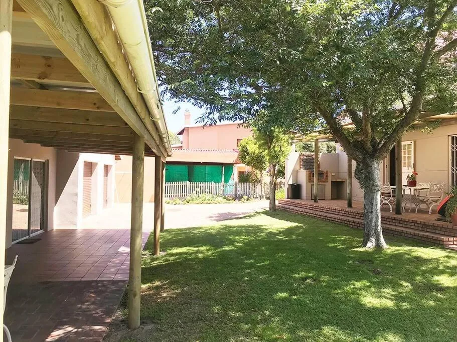 Shaded patio area with manicured lawn and large tree, adjacent buildings visible