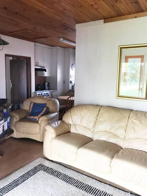 Cream leather sofa and armchair in open-plan living space with wooden ceiling