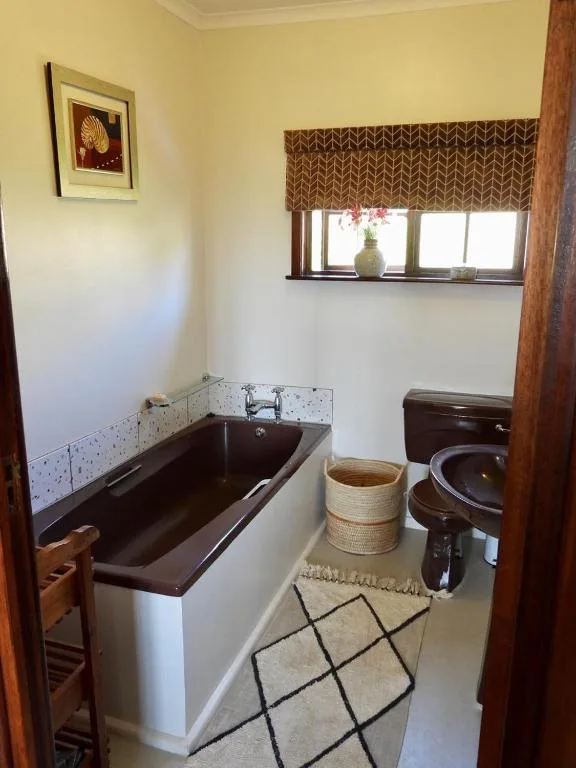 Bathroom with dark brown bathtub, white walls, patterned window blind