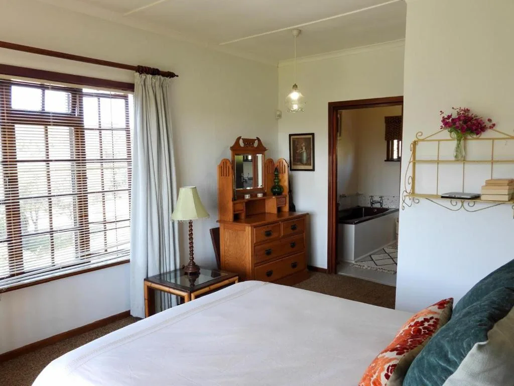 Bright bedroom with double bed, wooden dresser, and large windows