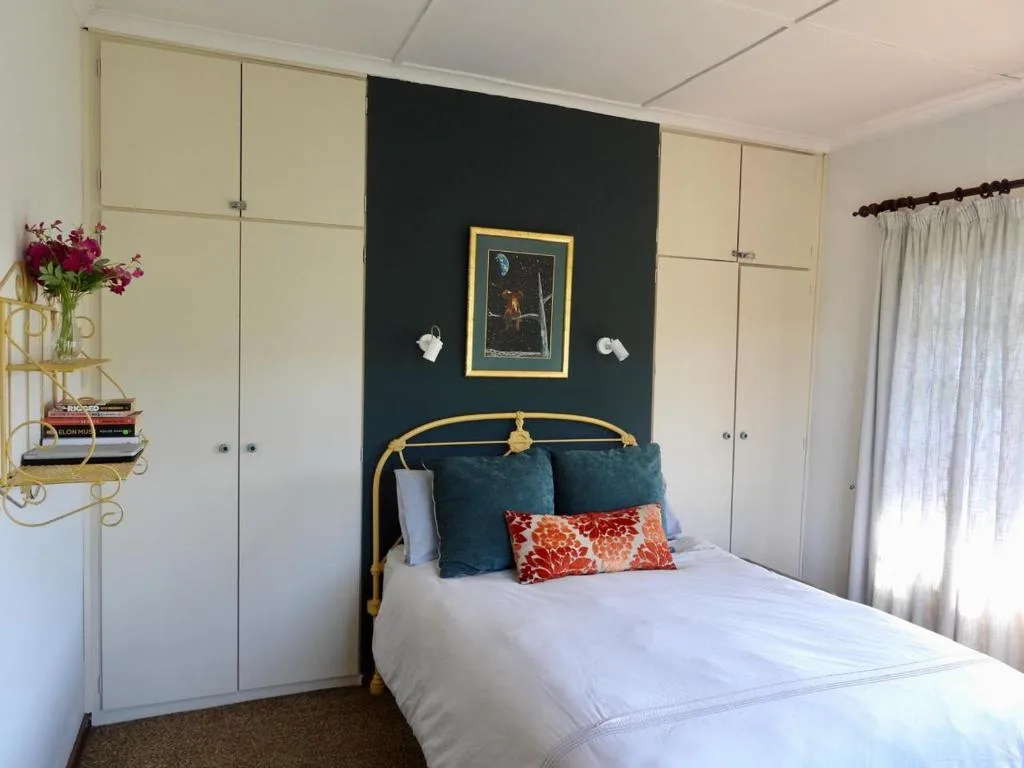 Bedroom with brass bed frame, teal accent wall, and cream storage cabinets