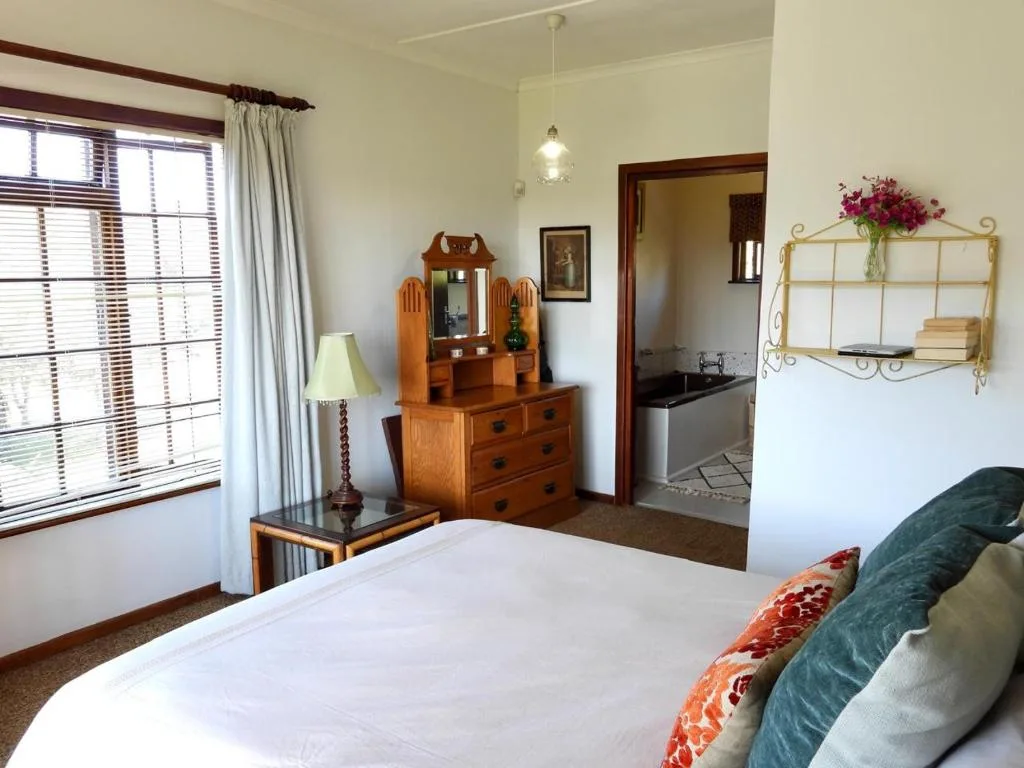 Bright bedroom with white bedding, wooden dresser, and garden views through windows