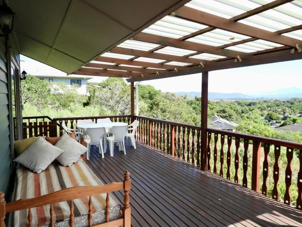 Covered wooden deck with lounge seating and dining table overlooking green landscape