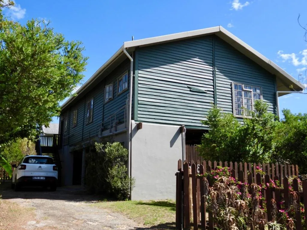 Modern elevated house with blue-green siding and wooden fence, parked car visible