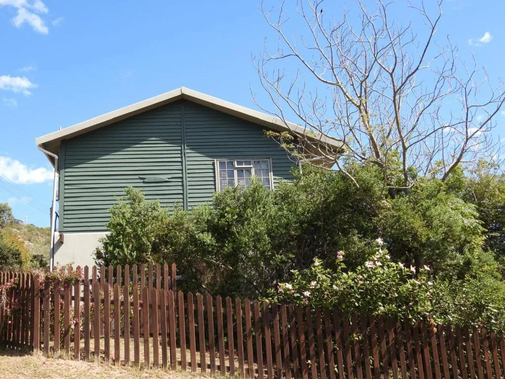 Green weatherboard cottage with wooden fence and surrounding garden vegetation