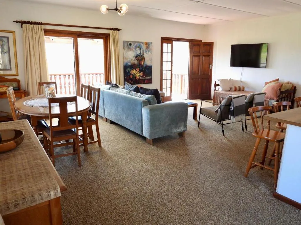 Open-plan lounge with blue sofa, dining table, TV, and deck access