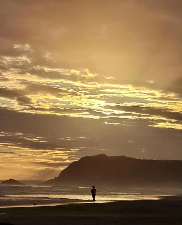Golden sunset over beach with silhouetted cliffs and surfer